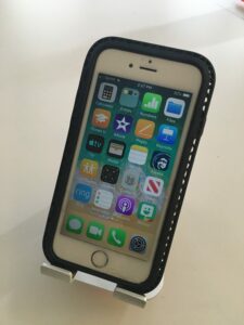 photograph of a small apple telephone with four columns across the top on its touch sensitive face with six rows down the bottom tilted to face the user with an aluminum support on a white desk.