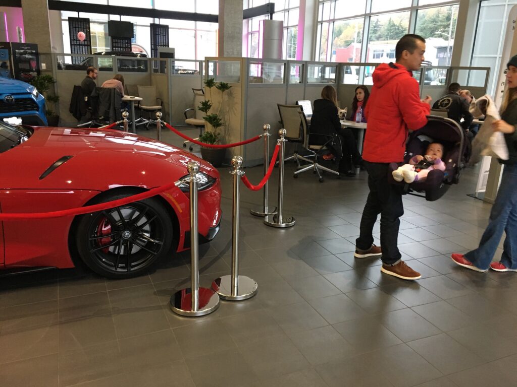 Red jacket dad holding baby in car seat in  auto dealer next to red car